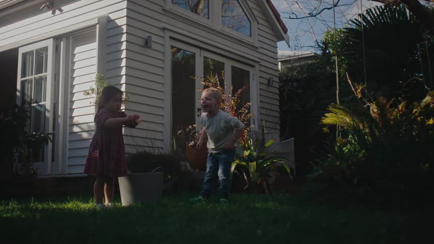 Two kids throwing water balls in the grassy backyard