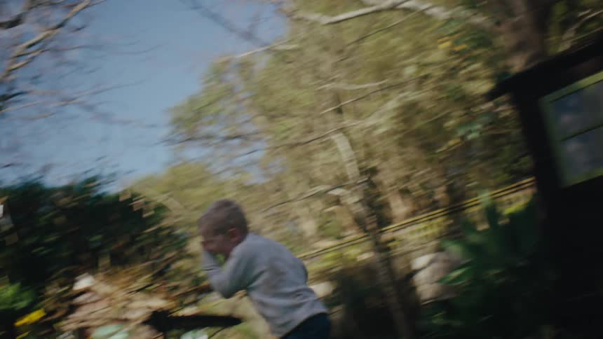 A little blond boy and a little girl are playing in a yard and both are holding toys in their hands and the little girl is walking forward