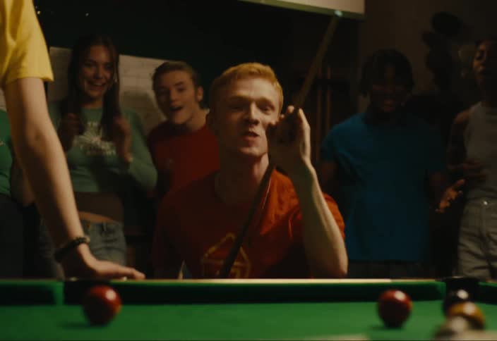 Man hitting a shot in pool with people cheering around him