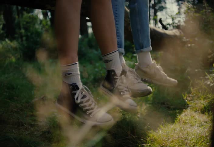 The legs of two people and one of the people is swinging his legs back and forth