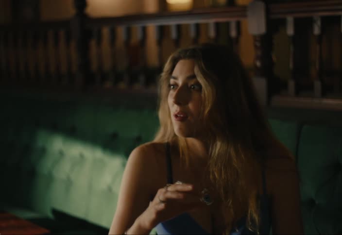 A woman with long blonde hair sits in a restaurant talking to someone