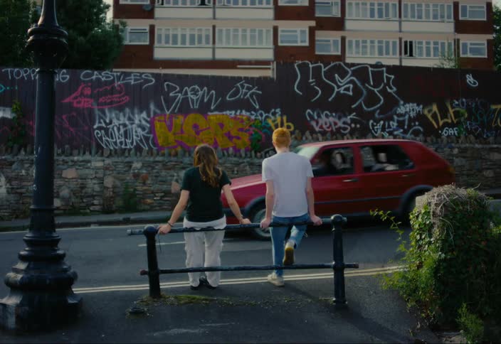 Woman and a man sitting watching a red car pass by on the street