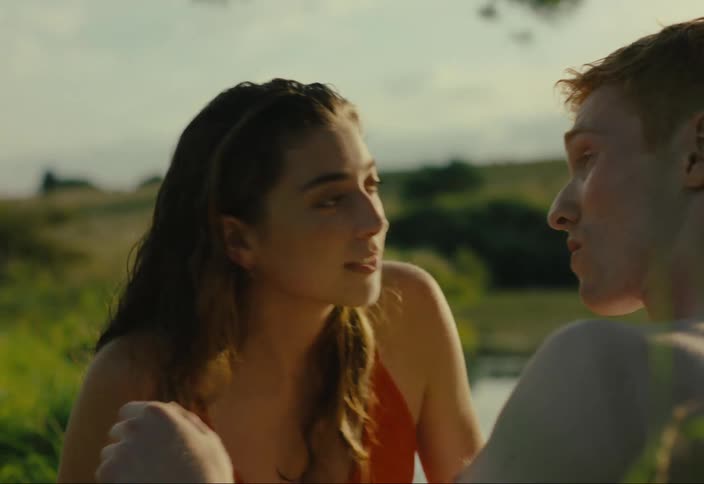 Woman kissing a man who smiles and continues to kiss while they are in a natural setting by a lake
