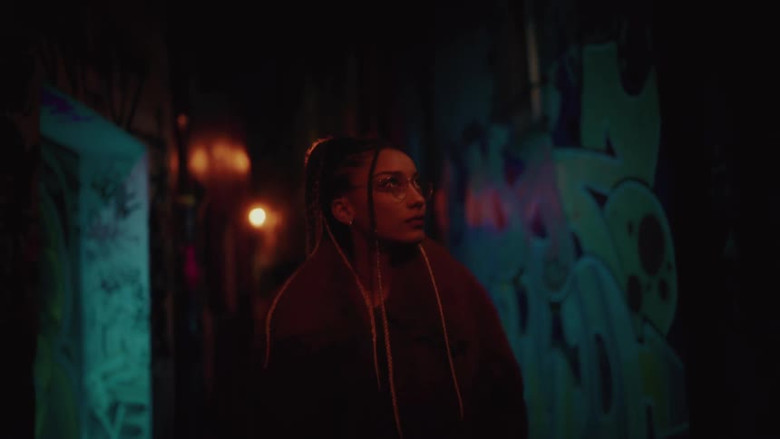 Woman in glasses and a coat walking in a dark alley with low lighting
