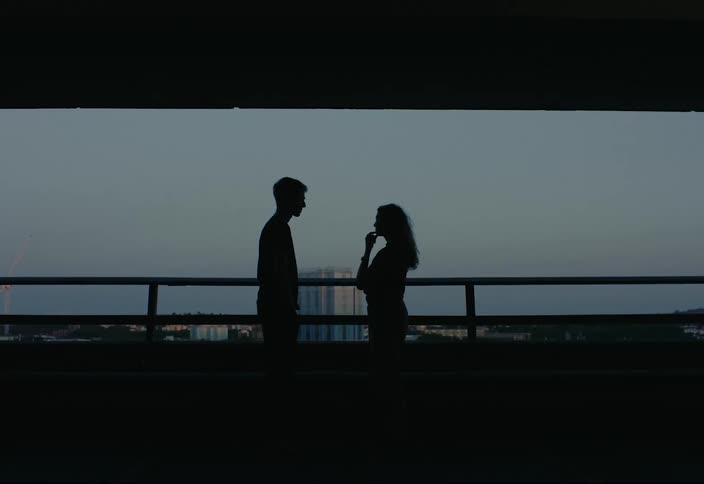 A man and woman talk under the dark overpass