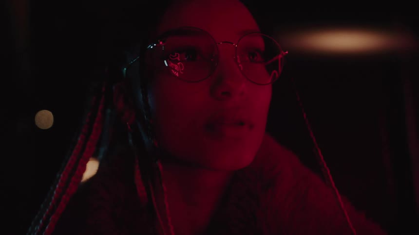 Closeup of a beautiful young woman with long braided hair and round glasses under soft red lights