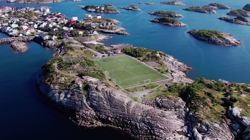 Aerial view of a football pitch on an island surrounded by sea with houses in the background