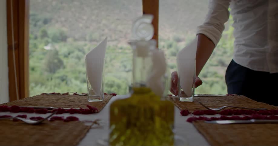 A man sets glasses with napkins in them on a dining room table