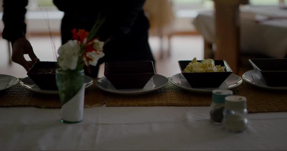 Person placing bowls of food on top of plates on a table