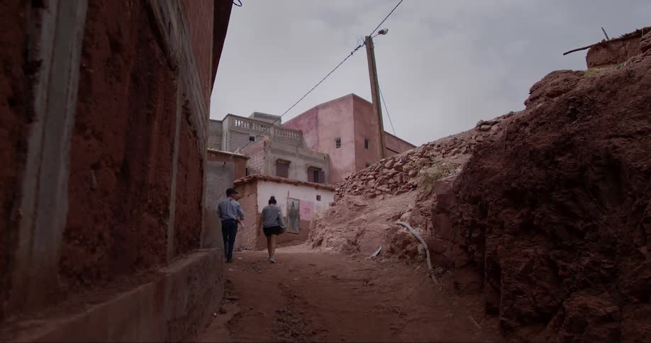 Two people walking on a dirt road with precarious houses