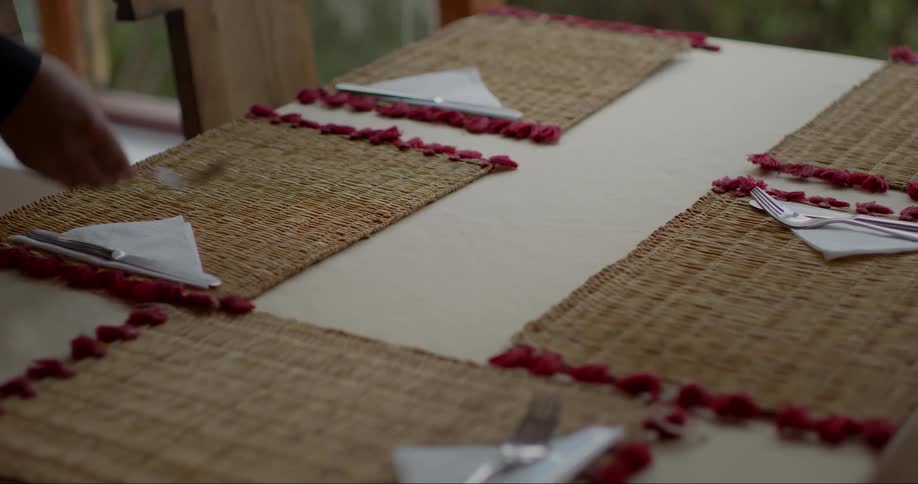 A person sets a table with woven placemats and silverware