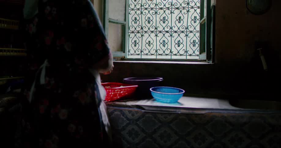 A woman stands in a kitchen and slices food into a red basket