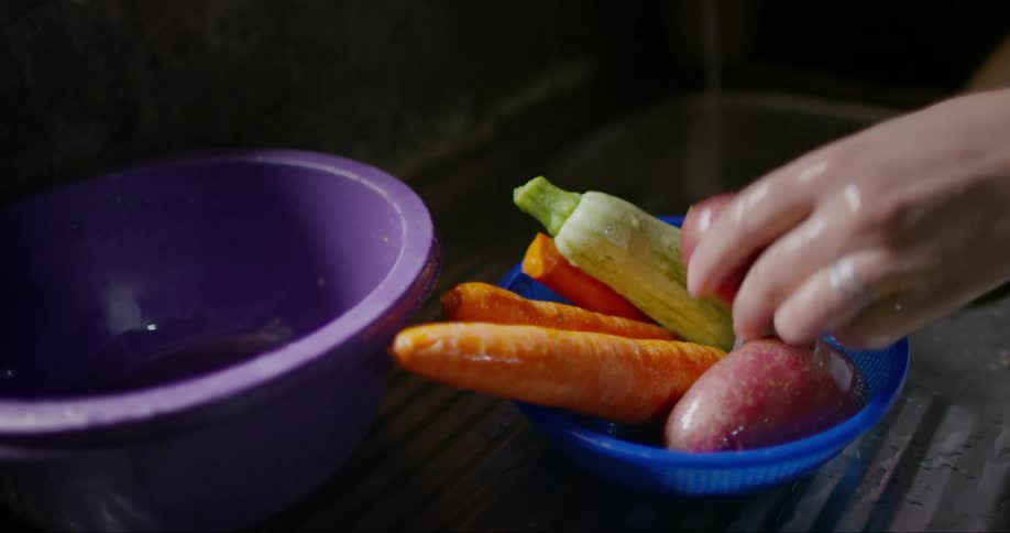 Person washing vegetables in the sink and placing them on top of a blue bowl