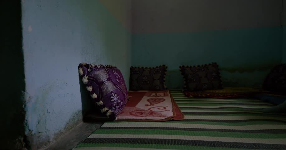 Corner of a room with a green and white striped rug on the floor and decorative pillows against the wall