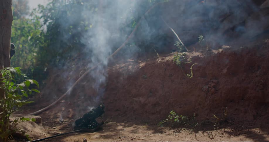Smoke rising from a small fire or smoldering object on the ground near a dirt embankment