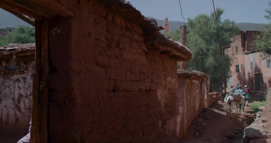 People with horses walking in an urban city with precarious mud houses and in the background hills and mountains