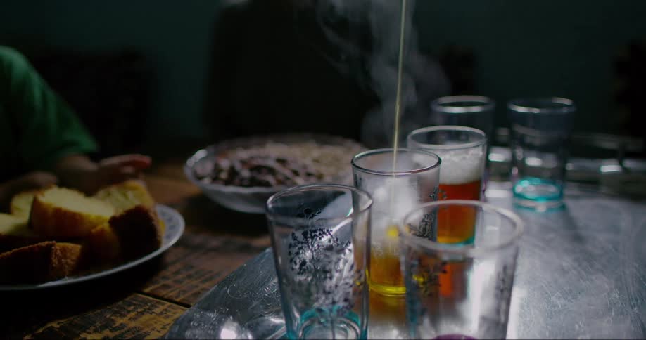 In a restaurant hot tea pours into a glass as a customer waits nearby