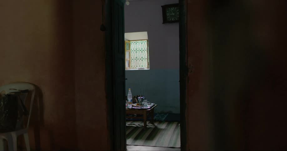A shadow of a person moves across a doorway through which food and drink sits on a table