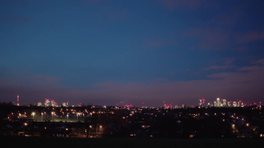 Bright lights illuminate the city skyline under a cloudy sky at night