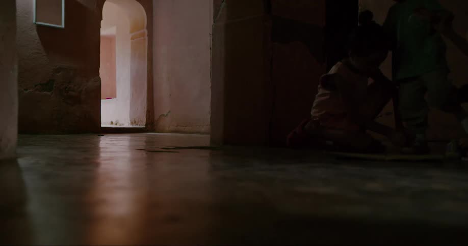 Children playing in a room and in the background a woman walking down a hallway