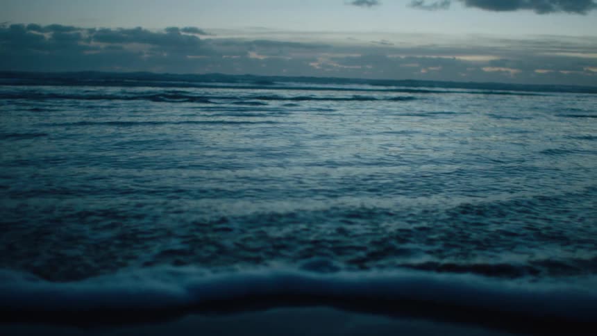 Ocean waves move to a coastal area under a cloudy sky