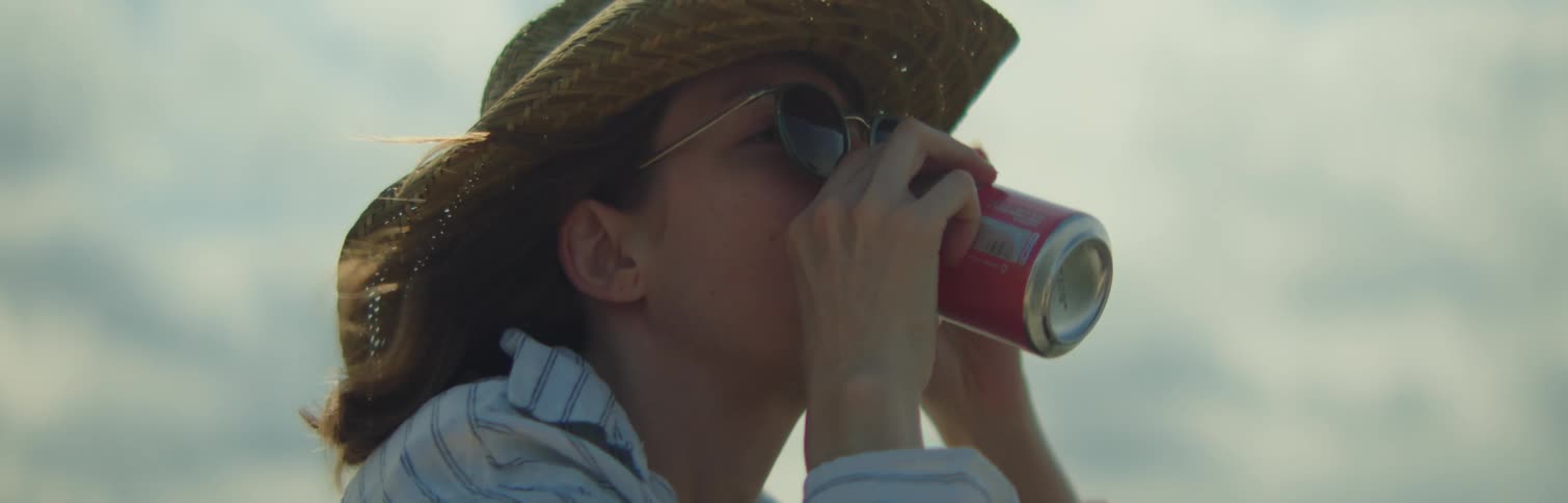 Woman in hat and sunglasses drinking from a can of soda