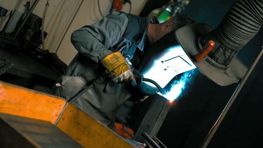 Welder man with protective helmet welding a metal sheet