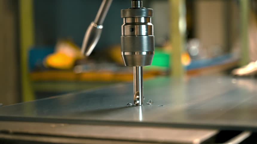 A drill bit drilling into a metal sheet creating a hole in the metal