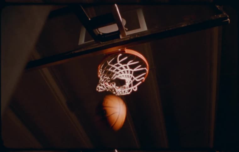 A basketball passing through a hoop net with the rim and backboard visible in the background
