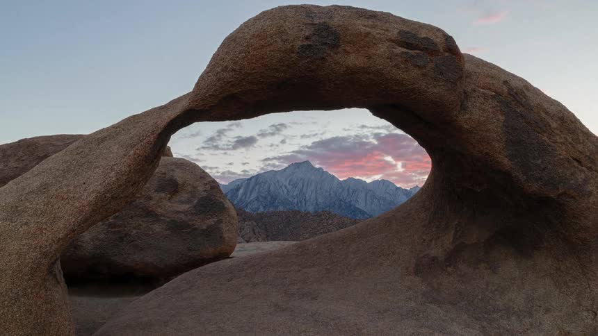 Natural rock arch formation with a clear view of a mountain range in the background