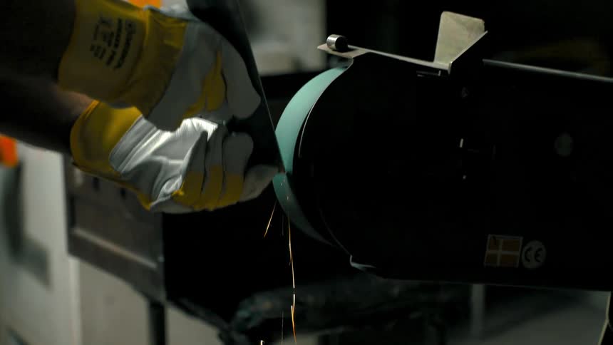 A person uses a grinding wheel to smooth a piece of metal