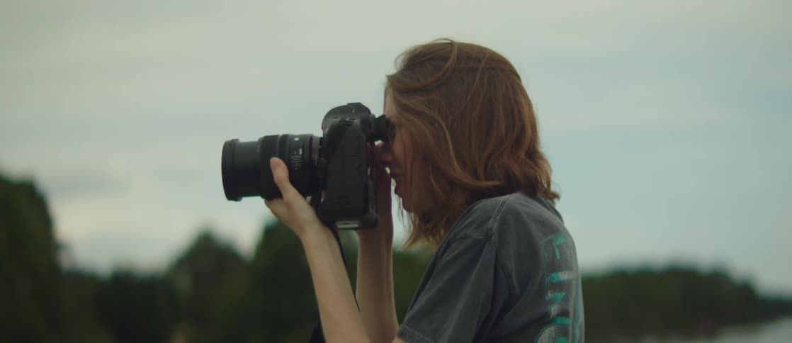 Female photographer using a professional camera in an outdoor setting with trees in the background