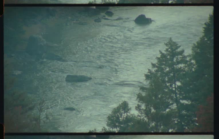 View from above of a river with rocks and conifers on the bank