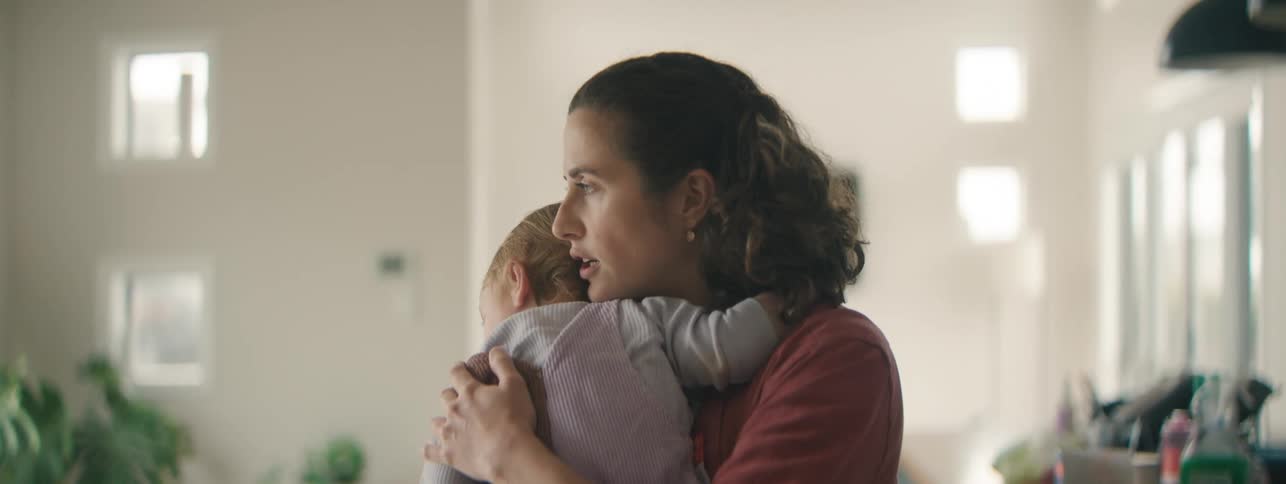A mother looks worried as she hugs her child tightly in a living room