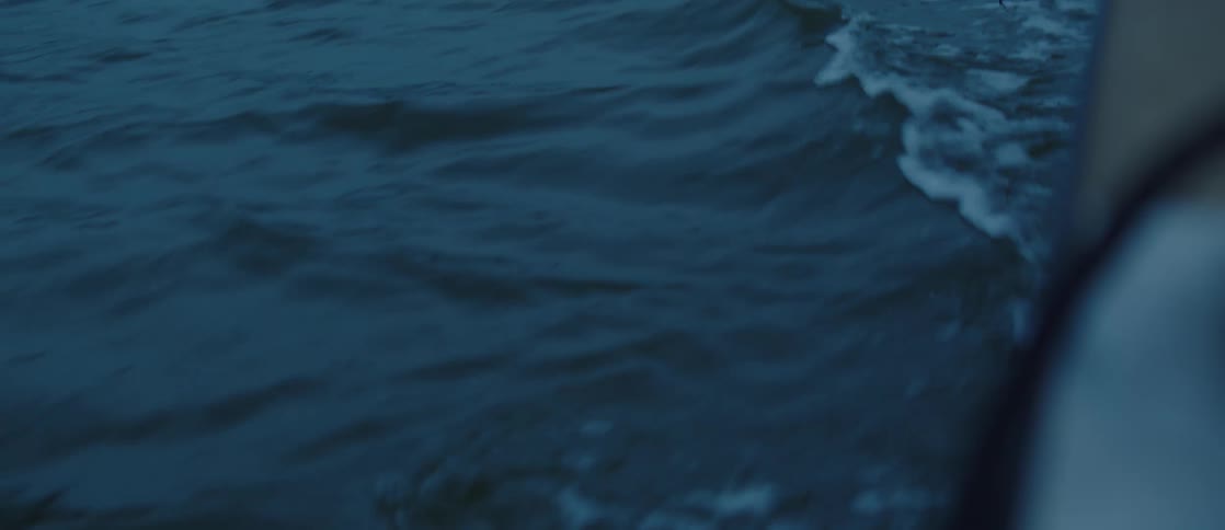 A corner of a boat is shown driving in an ocean