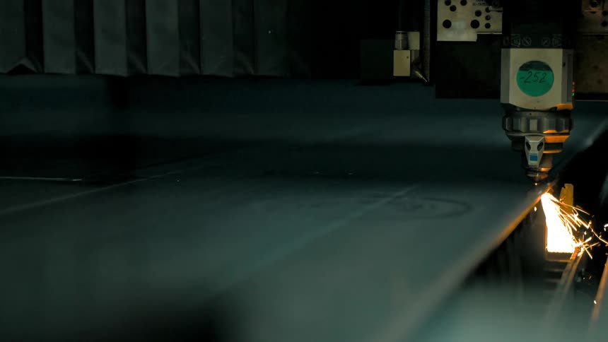 A large machine cuts through a sheet of metal and emits lots of sparks