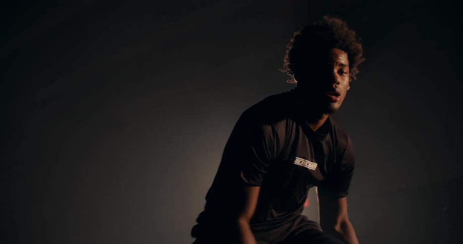 Man dribbles a basketball while outdoors at night in an area lit by a spotlight