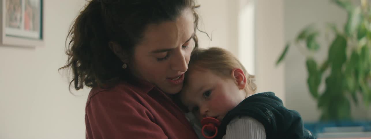 A mother embraces her son and rocks him back and forth while standing in a living room