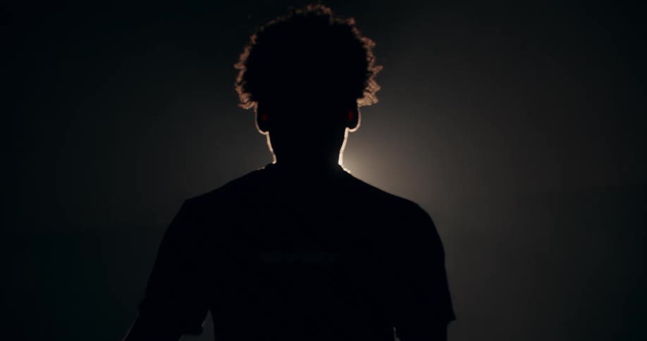 Silhouette of a man from behind with a light on his face doing basketball moves