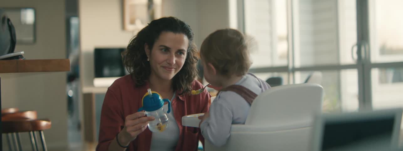 Woman feeding her child in a high chair scolds the toddler when they try to drop food on the floor
