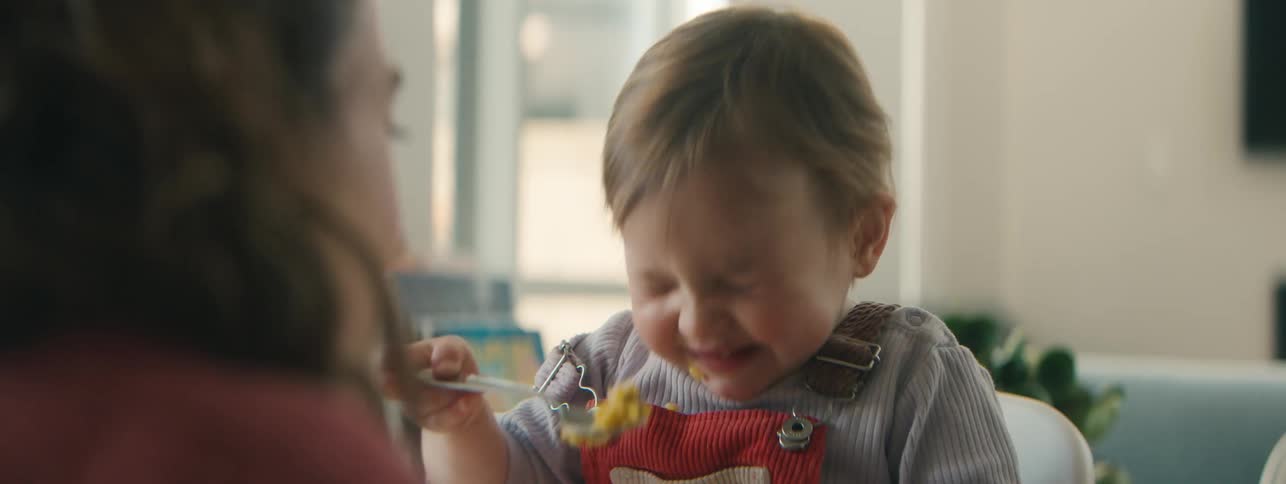 A child wearing red overalls and a striped shirt sitting at a table and eating with a spoon