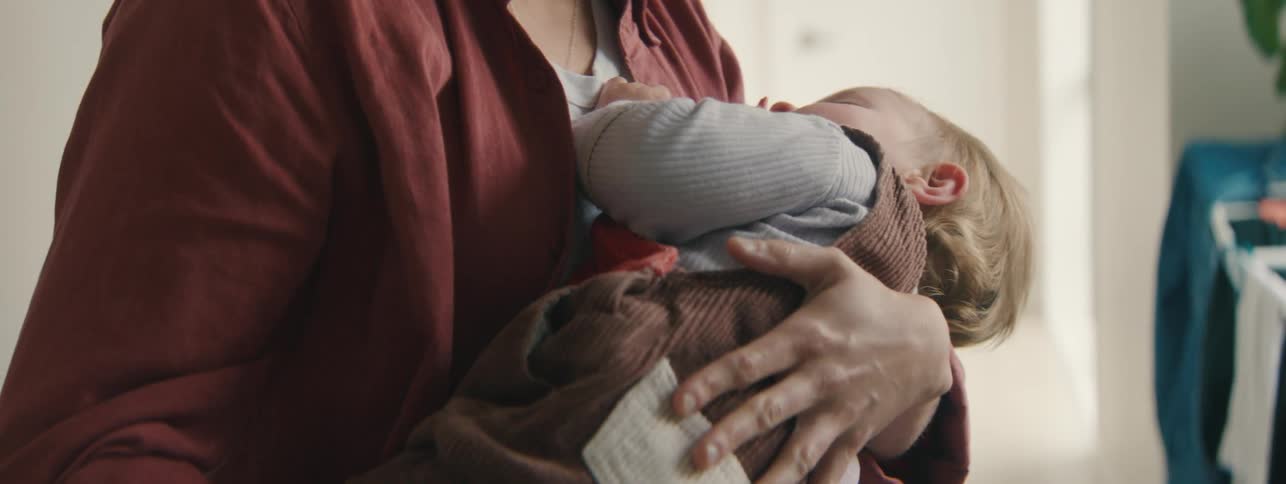 Mother holding her little daughter in her arms giving her a pacifier and putting her to sleep