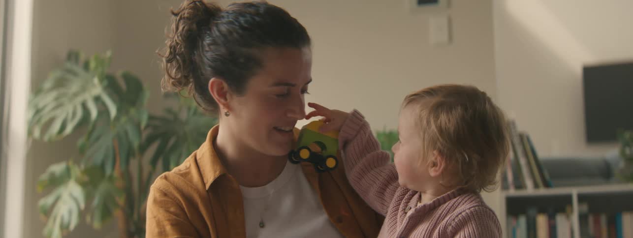 A mother laughs while her toddler son tries to play with her with a toy