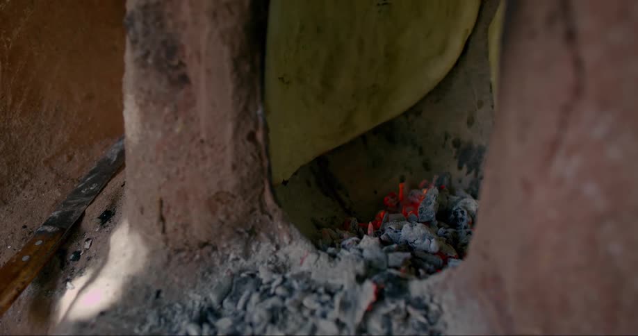 Bread baking inside a traditional clay oven with the dough adhered to the ovens wall while glowing embers at the base radiate heat slowly cooking the bread