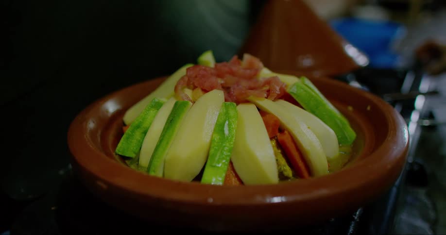 A person pours liquid into a clay pot filled with vegetables