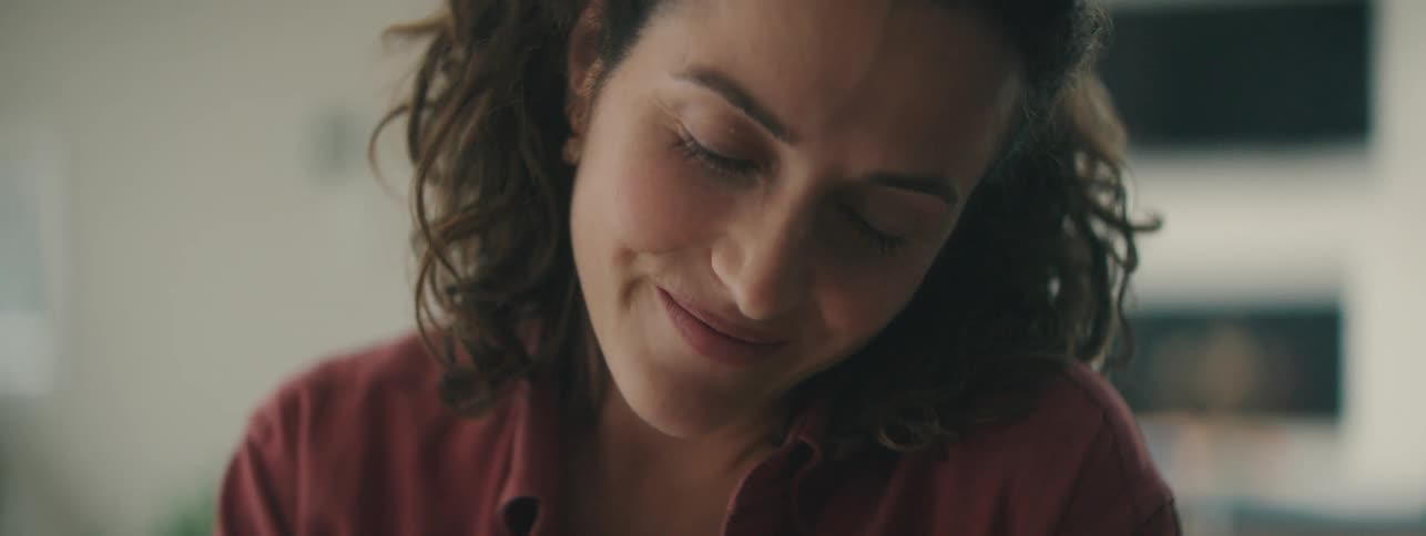 Woman with curly hair in red shirt smiling gently.