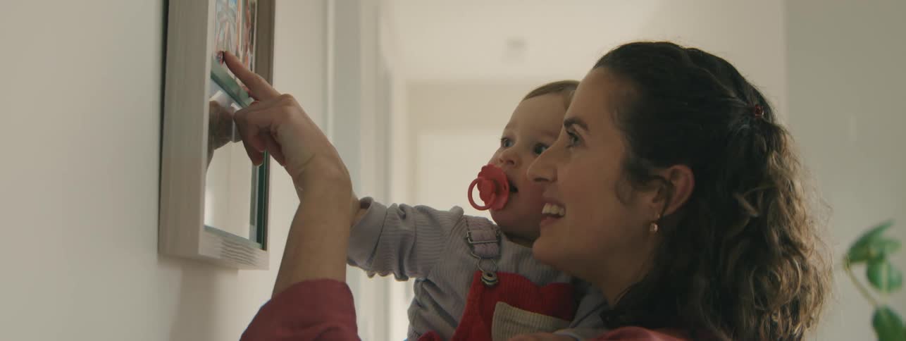 Mother pointing out people in a picture on the wall to her baby