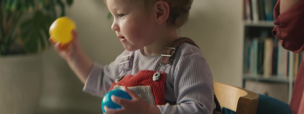 Little girl playing with balls at the table next to an adult