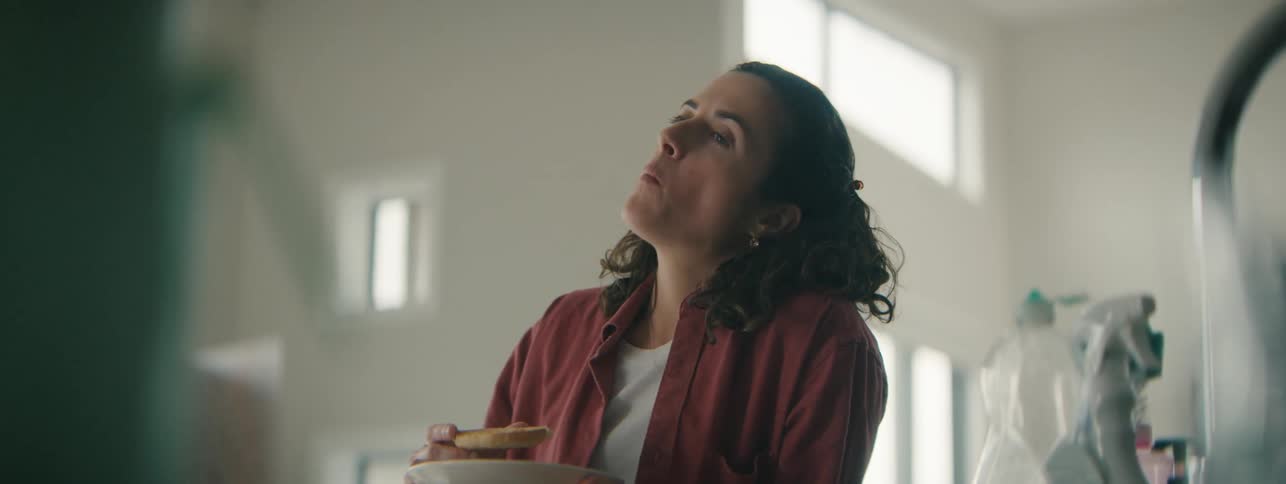 Exhausted young woman eating a snack in her kitchen.