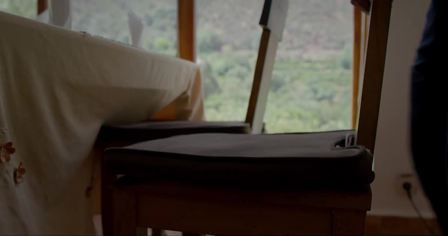 Man pushes chairs underneath a table in a dining room overlooking the mountain